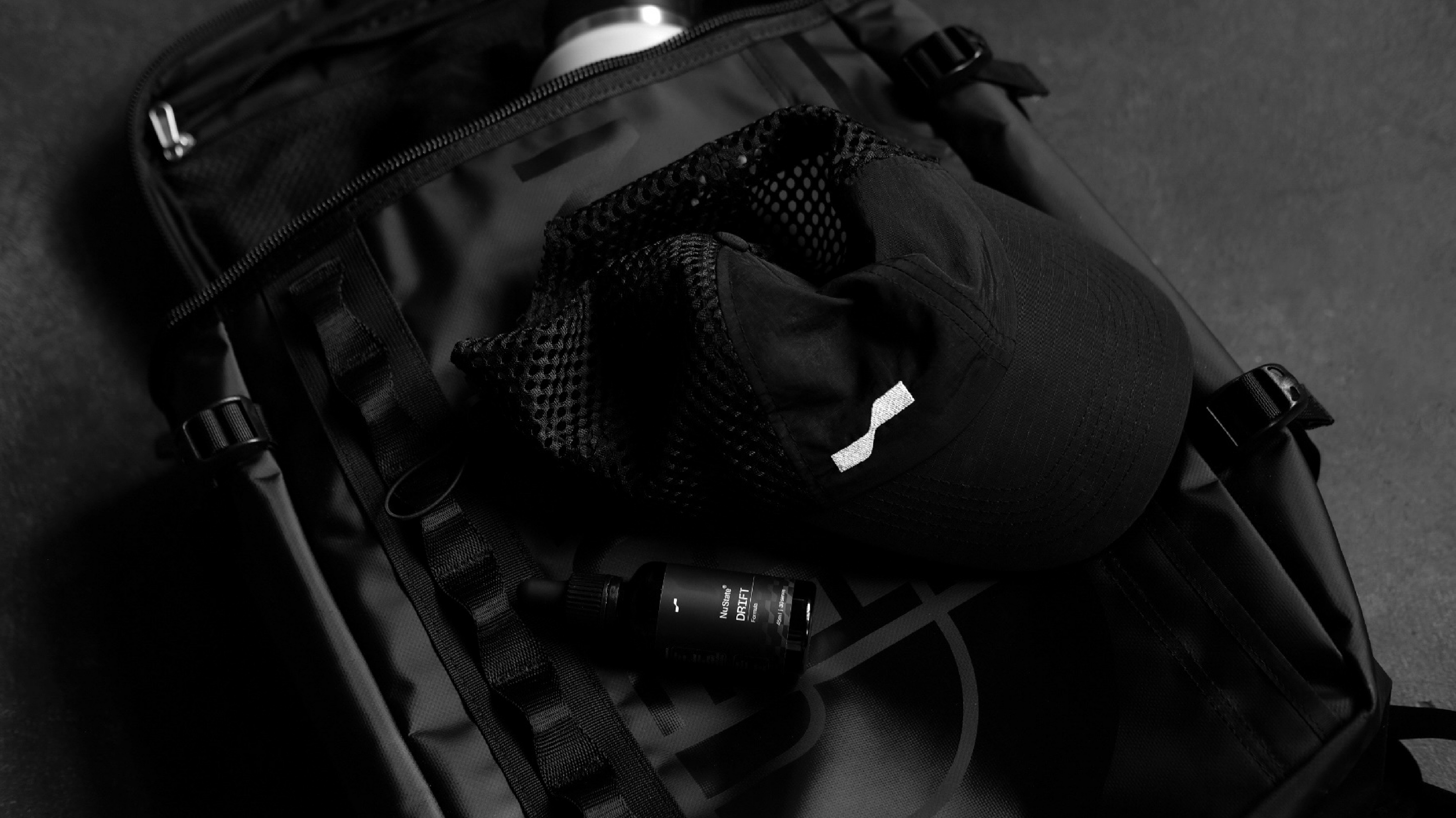 Black The North Face backpack with a Nu State cap and water bottle on a dark background